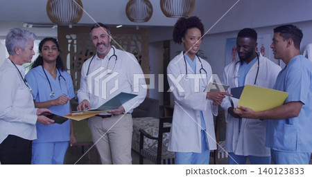 Reviewing charts, six staff in lounge wearing white coats holding folders, tablet, stethoscopes Reviewing charts, six staff in lounge wearing white coats holding folders, tablet, stethoscopes 140123833