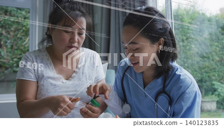 Guiding nurse in blue scrubs leaning near window at home, patient opening green cap bottle Guiding nurse in blue scrubs leaning near window at home, patient opening green cap bottle 140123835