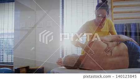 Leaning therapist in yellow top mobilizing shirtless male patient on treatment table near mirror Leaning therapist in yellow top mobilizing shirtless male patient on treatment table near mirror 140123845