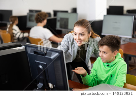 Smiling female teacher talking to happy student in computer class Smiling female teacher talking to happy student in computer class 140123921