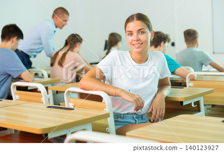 Cheerful girl student sitting at table and writing lectures Cheerful girl student sitting at table and writing lectures 140123927
