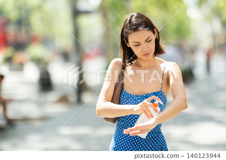 Young woman applying sunscreen on city street 140123944