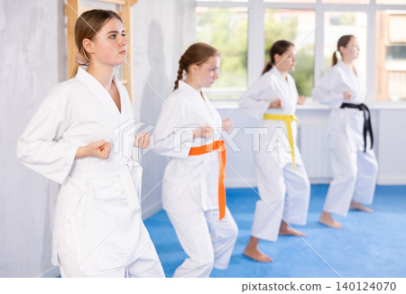 Team of teenage girls in kimonos stand in fighting stance during group karate training session Team of teenage girls in kimonos stand in fighting stance during group karate training session 140124070