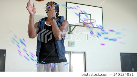 Tossing player wearing hoodie, sweats in gym with basketball, backboard, smartwatch, purple trails 140124081