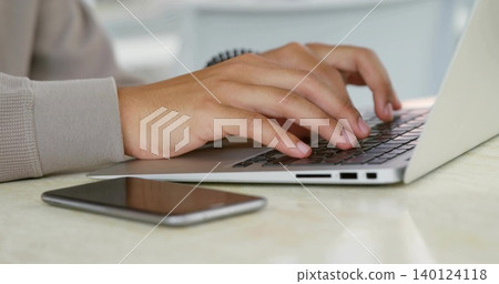 Typing male hands on silver laptop with visible ports at home, phone face-up, knit-sleeve wristband Typing male hands on silver laptop with visible ports at home, phone face-up, knit-sleeve wristband 140124118