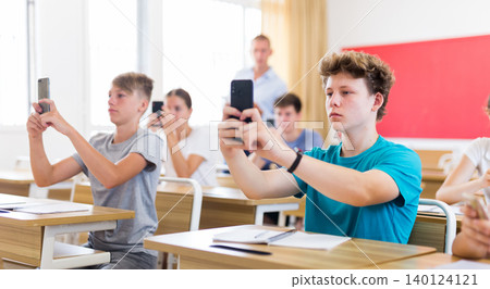 Teen pupils using mobile phones during lesson 140124121