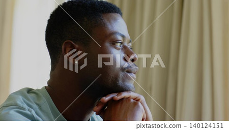 Gazing man wearing green tee, resting chin on hands at home, stud earring, curtains, copy space Gazing man wearing green tee, resting chin on hands at home, stud earring, curtains, copy space 140124151