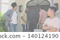 Smiling man in pink T-shirt standing arms crossed at stucco entry, holding passport and suitcases 140124190
