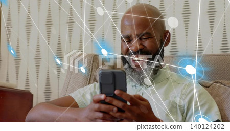 Smiling man in green shirt holding smartphone, browsing on beige sofa at home, network overlays Smiling man in green shirt holding smartphone, browsing on beige sofa at home, network overlays 140124202