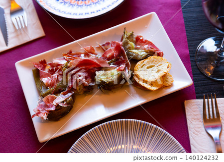 Dish of fried artichoke flowers and slices of ham is served on plate 140124232