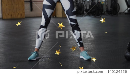 Standing female lower body displaying wide stance at gym, patterned leggings and teal sneakers Standing female lower body displaying wide stance at gym, patterned leggings and teal sneakers 140124356