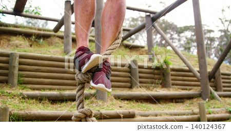 Balancing man legs and feet wrapping around braided rope on terraced log bank with maroon sneakers Balancing man legs and feet wrapping around braided rope on terraced log bank with maroon sneakers 140124367