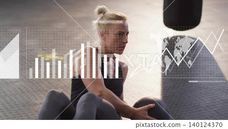Holding medicine ball, woman twisting in gym, wearing black tank top, punching bag and graphs Holding medicine ball, woman twisting in gym, wearing black tank top, punching bag and graphs 140124370