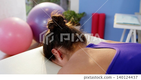 Lying woman wearing purple top getting rehab on padded table with exercise balls and foam rollers Lying woman wearing purple top getting rehab on padded table with exercise balls and foam rollers 140124437