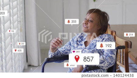Smiling woman in wheelchair leaning toward shutters at home, in blue top, viewing alerts by table Smiling woman in wheelchair leaning toward shutters at home, in blue top, viewing alerts by table 140124438