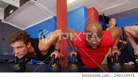 Performing man in red sleeveless shirt pushing up on kettlebell handles at gym with wrist tracker Performing man in red sleeveless shirt pushing up on kettlebell handles at gym with wrist tracker 140124478