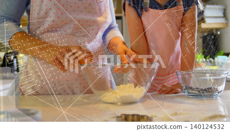 Mixing adult and child in aprons stirring dough on kitchen counter, with glass bowl, cookie cutter 140124532