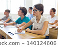 High school student teenage girl studying in college with classmates, making notes of teacher lecture 140124606