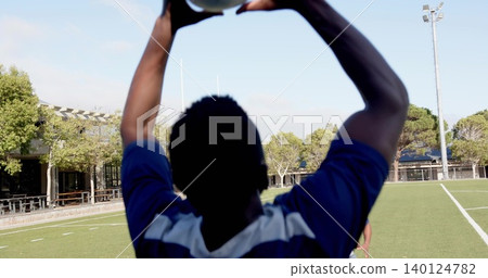 Holding soccer player in blue jersey raising soccer ball overhead on grass pitch, goalposts Holding soccer player in blue jersey raising soccer ball overhead on grass pitch, goalposts 140124782
