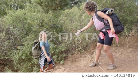Two women hikers assisting on sloped dirt trail, carrying packs, rolled pad, flannel tied at waist Two women hikers assisting on sloped dirt trail, carrying packs, rolled pad, flannel tied at waist 140124819