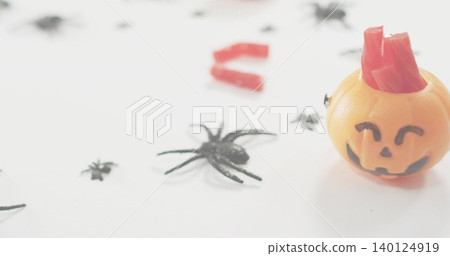 Showing orange pumpkin bucket holding red candy sticks on white desk with black spiders, copy space Showing orange pumpkin bucket holding red candy sticks on white desk with black spiders, copy space 140124919