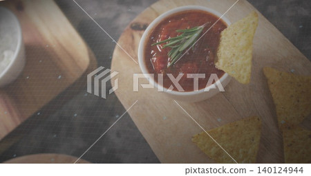 Displaying white bowl holding tomato salsa with rosemary on wooden board in kitchen, tortilla chips 140124944