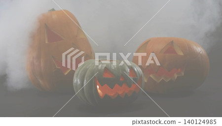 Glowing three carved pumpkins emitting warm inner light on dark tabletop with drifting smoke Glowing three carved pumpkins emitting warm inner light on dark tabletop with drifting smoke 140124985