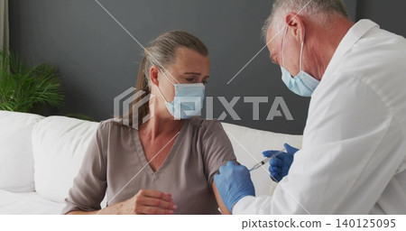 Injecting doctor in lab coat, blue gloves vaccinating mature woman at home on couch, syringe, masks Injecting doctor in lab coat, blue gloves vaccinating mature woman at home on couch, syringe, masks 140125095