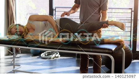 Supporting therapist guiding patient on table in tank top and leggings at rehab, waveform overlay Supporting therapist guiding patient on table in tank top and leggings at rehab, waveform overlay 140125097