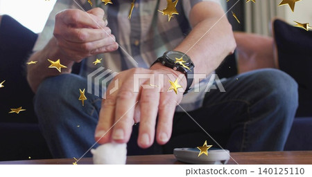 Reaching seated senior handling small white object on living room table, in plaid shirt and jeans Reaching seated senior handling small white object on living room table, in plaid shirt and jeans 140125110