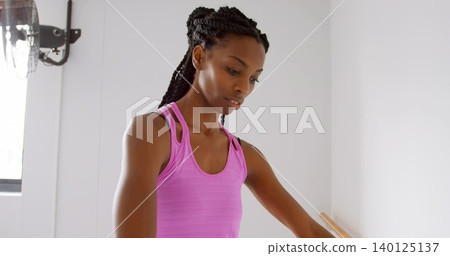 Practicing midadult woman wearing hot pink tank top holding wooden barre in small studio, with fan Practicing midadult woman wearing hot pink tank top holding wooden barre in small studio, with fan 140125137