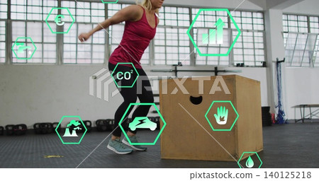 Doing plyo, mid-adult woman wearing maroon top and black leggings at gym with plyo box, kettlebells Doing plyo, mid-adult woman wearing maroon top and black leggings at gym with plyo box, kettlebells 140125218