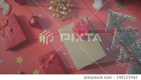 Displaying kraft-paper gift box resting on red surface, with red bows, gold bow, snowy trees Displaying kraft-paper gift box resting on red surface, with red bows, gold bow, snowy trees 140125482