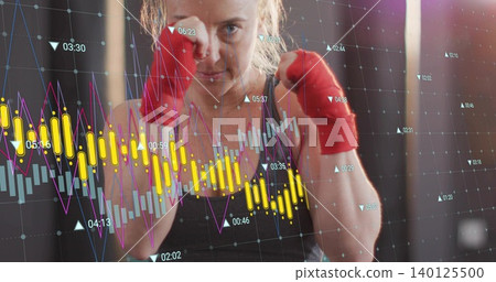 Boxing woman wearing dark tank holding fists up at gym, with red wraps and data overlay Boxing woman wearing dark tank holding fists up at gym, with red wraps and data overlay 140125500