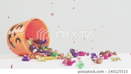 Spilling orange jack-o'-lantern bucket across white tabletop studio with foil candies, copy space Spilling orange jack-o'-lantern bucket across white tabletop studio with foil candies, copy space 140125515