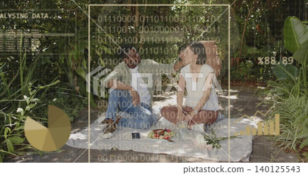 Sitting couple wearing casual clothes viewing AR data overlays on blanket in garden with smartphone Sitting couple wearing casual clothes viewing AR data overlays on blanket in garden with smartphone 140125543