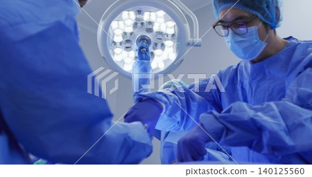 Operating surgical team wearing blue gowns, masks, gloves, working in operating room with LED light Operating surgical team wearing blue gowns, masks, gloves, working in operating room with LED light 140125560