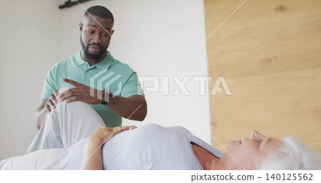 Bending male caregiver wearing green polo shirt supporting senior woman's leg on bed, copy space Bending male caregiver wearing green polo shirt supporting senior woman's leg on bed, copy space 140125562