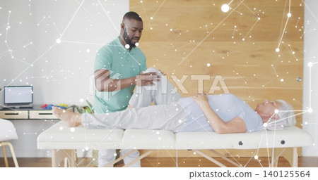 Bending therapist supporting senior patient right knee on therapy table, in green polo, laptop left Bending therapist supporting senior patient right knee on therapy table, in green polo, laptop left 140125564