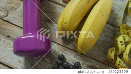Displaying purple dumbbell with ripe bananas on wood plank, showing yellow tape and blueberries 140125599