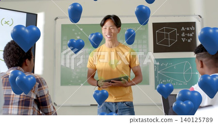 Presenting pupil wearing yellow tee, jeans holding tablet in class with periodic table, blue hearts Presenting pupil wearing yellow tee, jeans holding tablet in class with periodic table, blue hearts 140125789