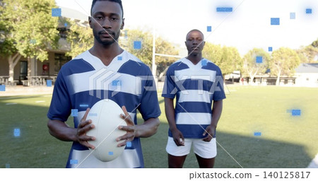 Holding white rugby ball, player posing on pitch, wearing navy jersey, goalposts and blue squares Holding white rugby ball, player posing on pitch, wearing navy jersey, goalposts and blue squares 140125817