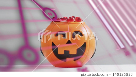 Sitting orange jack-o'-lantern bucket holding red gummies on white tabletop, pink reflections 140125853