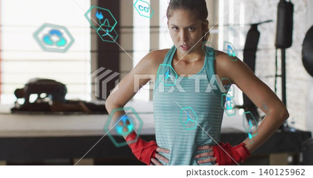Standing female athlete posing hands on hips in boxing ring, wearing teal tank and red wraps Standing female athlete posing hands on hips in boxing ring, wearing teal tank and red wraps 140125962