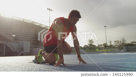 Kneeling runner wearing red tank, black shorts, neon shoes on blue track showing blocks and tracker Kneeling runner wearing red tank, black shorts, neon shoes on blue track showing blocks and tracker 140125990
