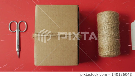 Displaying brown box wrapped with jute twine on red craft table with scissors, spool, tag Displaying brown box wrapped with jute twine on red craft table with scissors, spool, tag 140126048