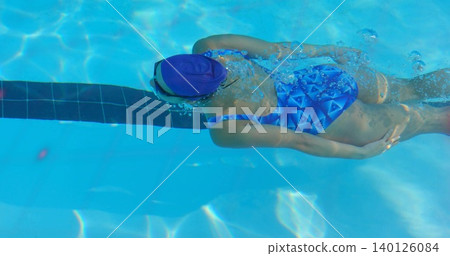 Gliding female swimmer wearing purple cap and goggles with blue suit in pool, passing lane stripe Gliding female swimmer wearing purple cap and goggles with blue suit in pool, passing lane stripe 140126084