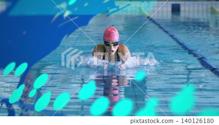 Swimming female swimmer in dark suit pushing forward at pool, with pink cap, goggles, bokeh 140126180