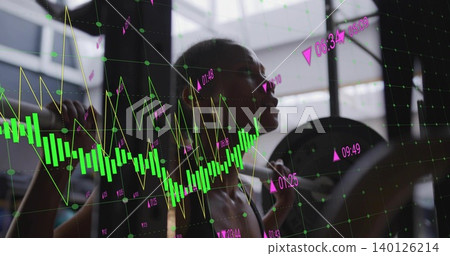 Holding barbell, mid-adult woman in sportswear squatting at gym with weight plate and chart overlay 140126214
