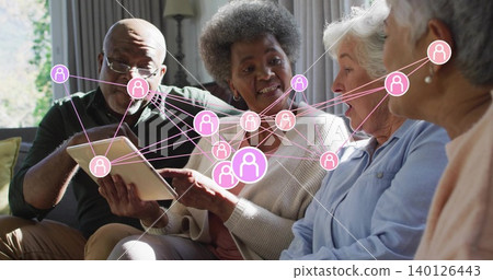Gathering group of four senior adults viewing tablet on living-room sofa, with pink network overlay Gathering group of four senior adults viewing tablet on living-room sofa, with pink network overlay 140126443